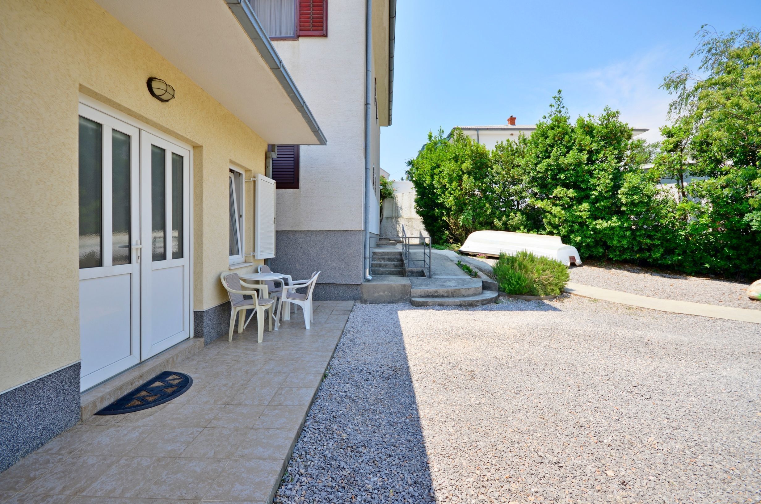 A building with a covered outdoor seating area, a staircase leading to a second floor, and a gravel driveway.
