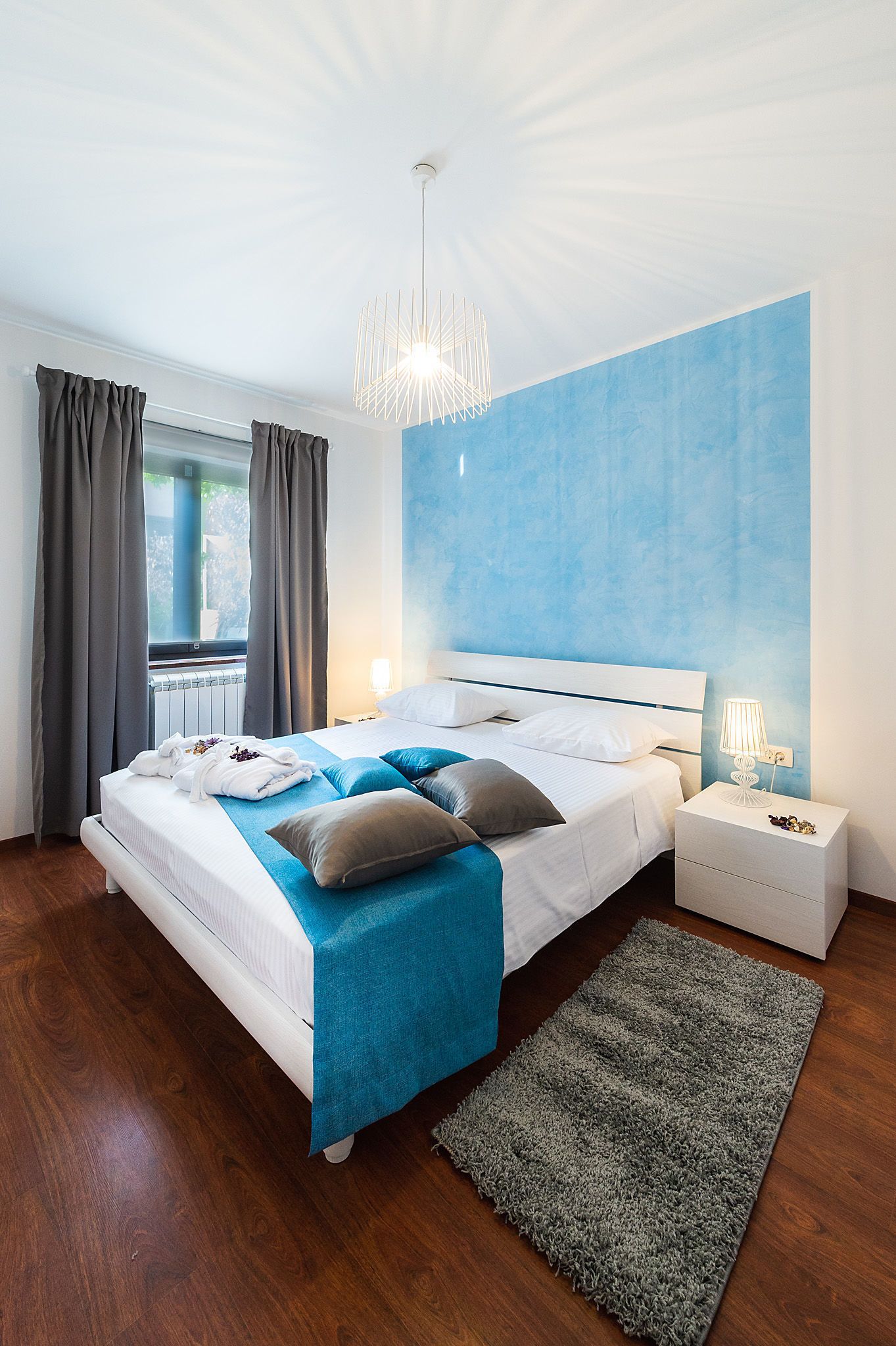 Een moderne slaapkamer met een groot bed, een nachtkastje, een blauwe accentmuur en uitzicht op de omgeving.
