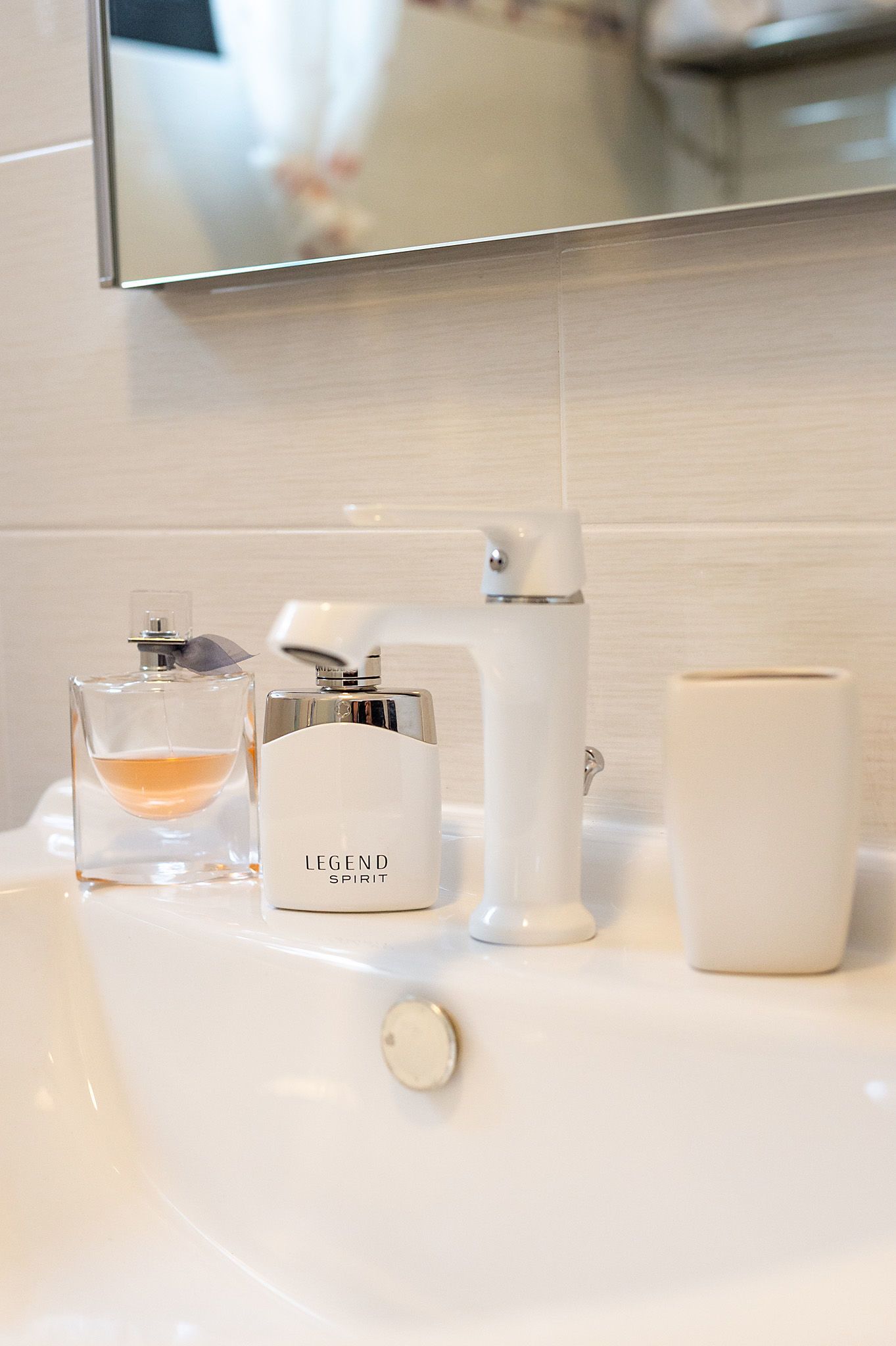 A bathroom sink with a mirror, a bottle of 'Legend Spirit' cologne, a white electric razor, and a white ceramic mug.