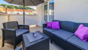 A balcony with wicker furniture, including a sofa and chairs, and a table with a candle. - Apartments Toni (Banjol)