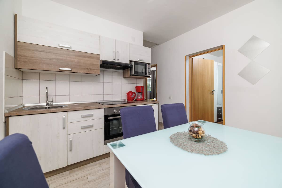 A modern kitchen with white cabinets, a microwave, and a coffee maker. There is a dining table with chairs and a vase of flowers.