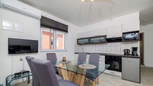 A modern kitchen with a glass dining table, purple chairs, and a built-in microwave. - Apartments Toni (Banjol)