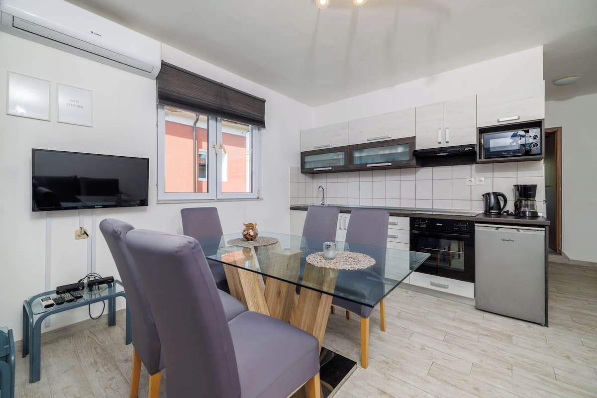 A modern kitchen with a glass dining table, purple chairs, and a built-in microwave.