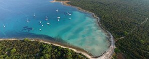 An aerial view of a coastal area with clear turquoise waters, boats, and a dense forested coastline.