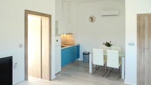 Een moderne keuken met blauwe kastjes, een eethoek met witte stoelen en een televisie op een witte console.