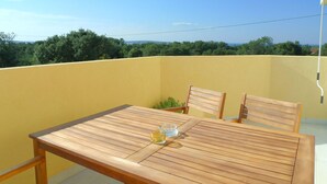 Een houten tafel met stoelen op een balkon met een gele muur en uitzicht op bomen en bergen.
