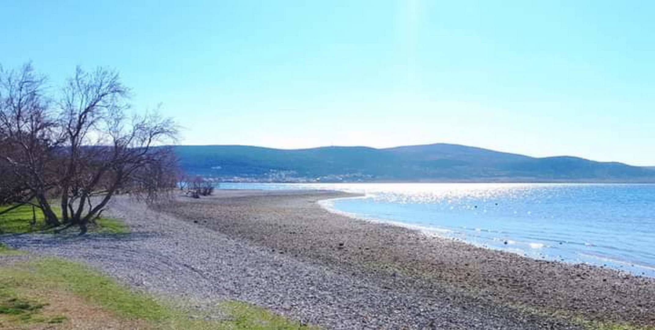Une plage de galets, avec un ciel dégagé et des montagnes à l’horizon.