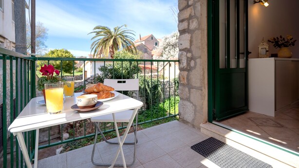 Un balcon avec une table préparée pour le petit-déjeuner, comprenant des croissants, une tasse de café et un verre de jus d’orange.