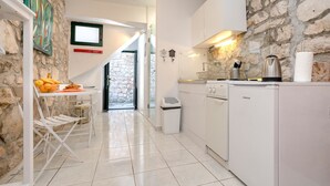 Une cuisine moderne avec des meubles blancs, un mur en pierre et un coin repas comprenant une table et des chaises.