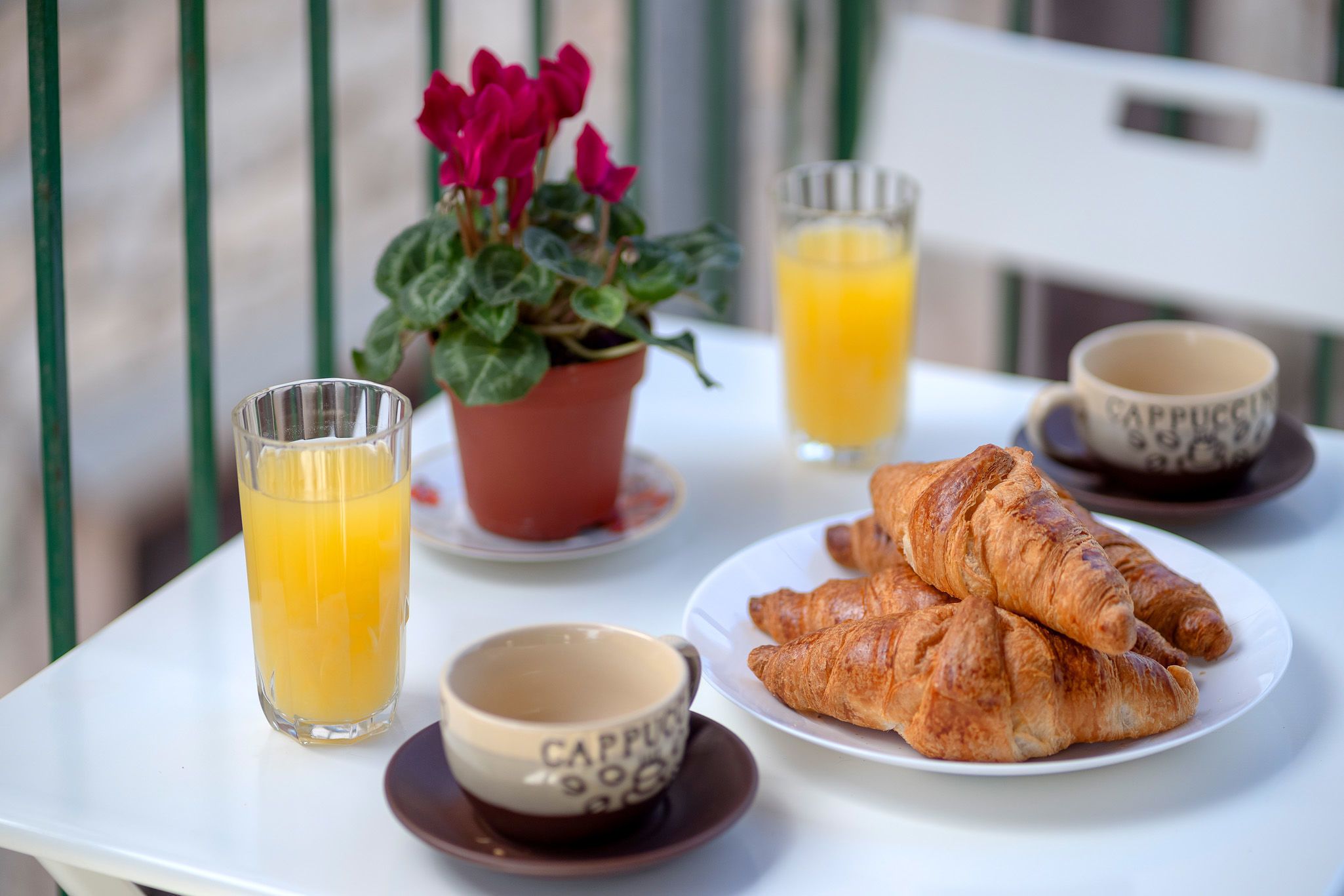 A table with croissants, a glass of orange juice, a cup of coffee, and a potted plant.