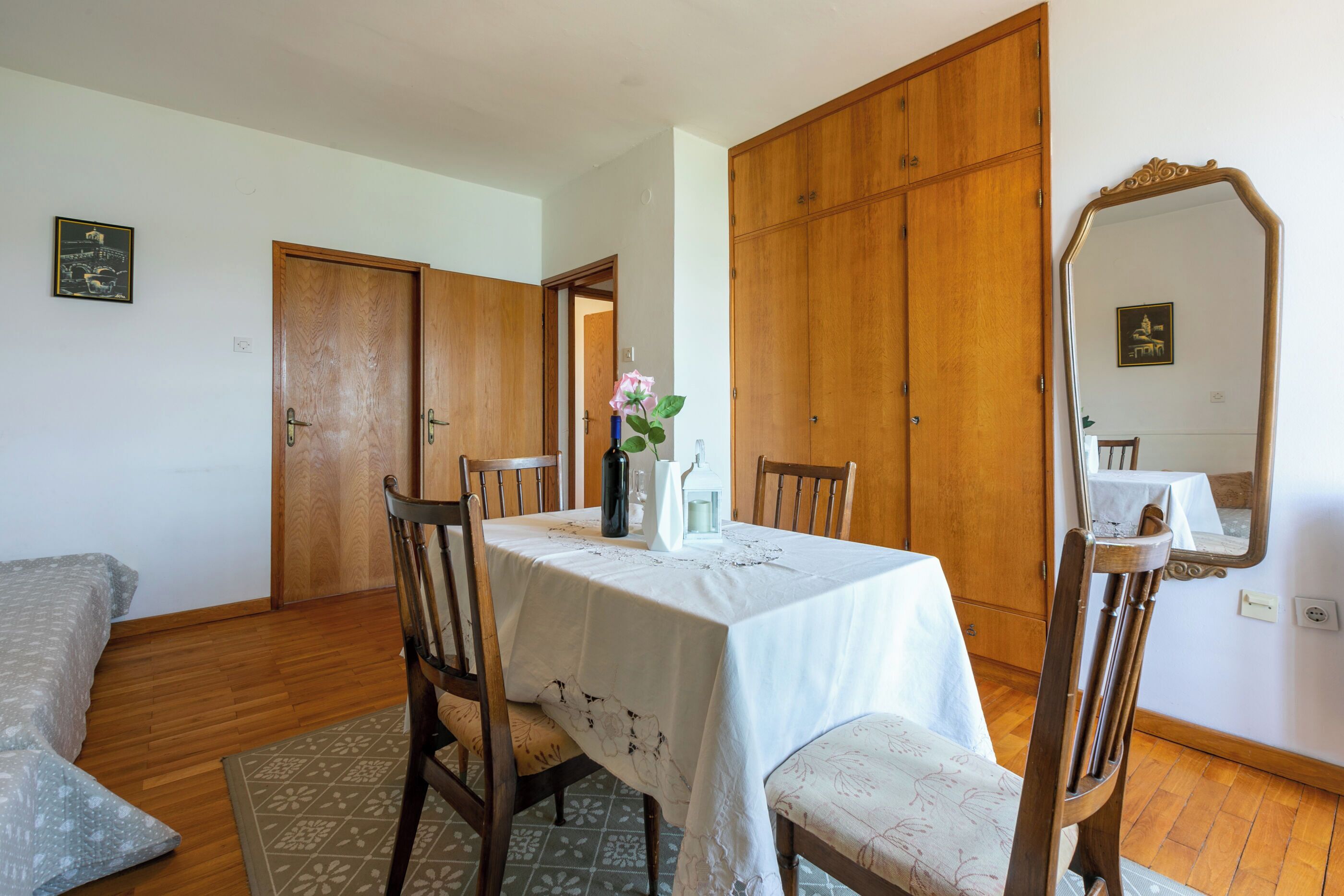 Zona pranzo con tavolo imbandito per quattro, sedie in legno, un vaso con fiori e uno specchio a parete.