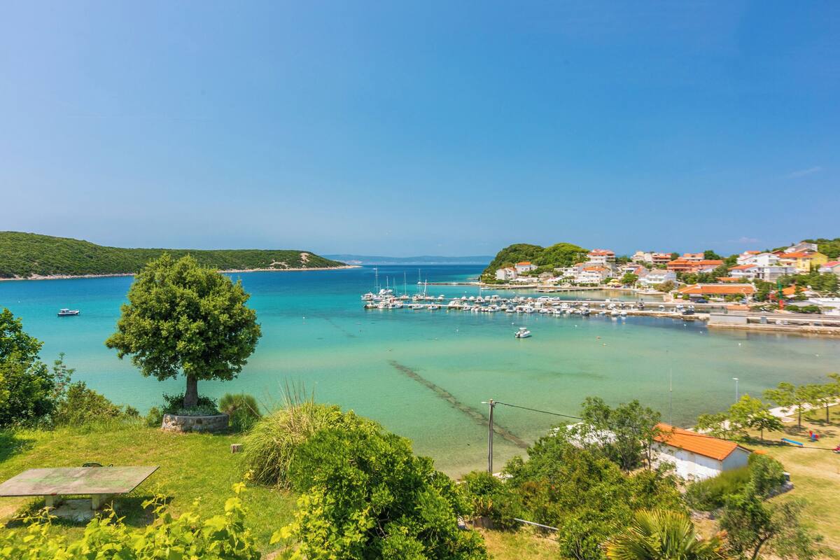 A coastal town with clear turquoise waters, a marina with boats, and lush greenery.