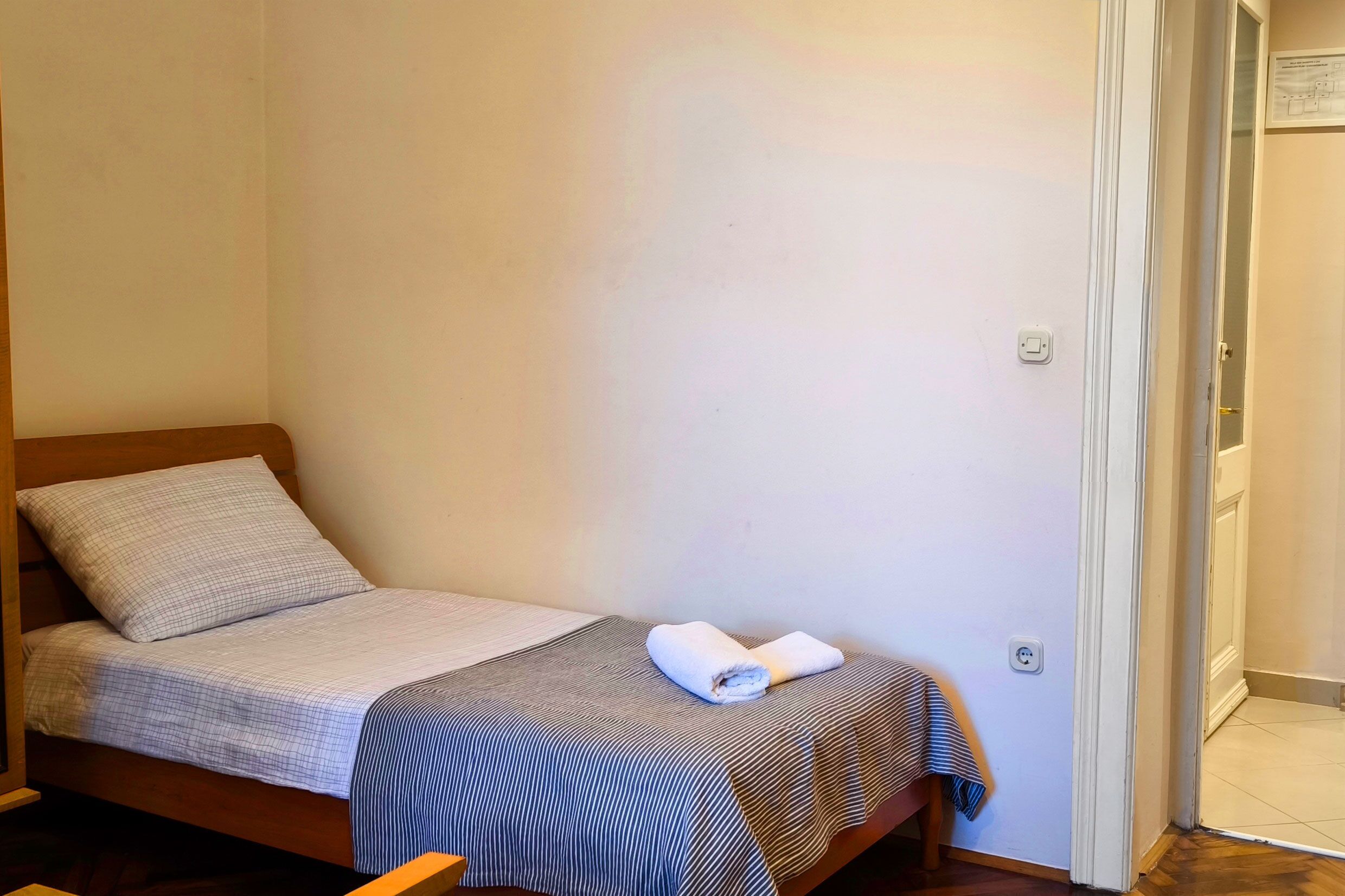 Een enkel bed met een gestreept dekbedovertrek en een opgerolde handdoek erop.