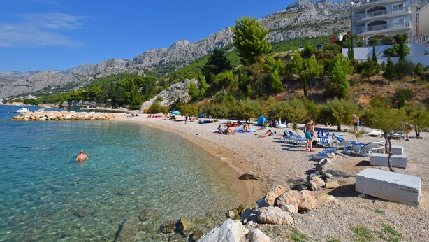 Ein Strand mit klarem Wasser, felsigem Ufer und einem Gebäude mit Balkonen mit Blick aufs Meer.