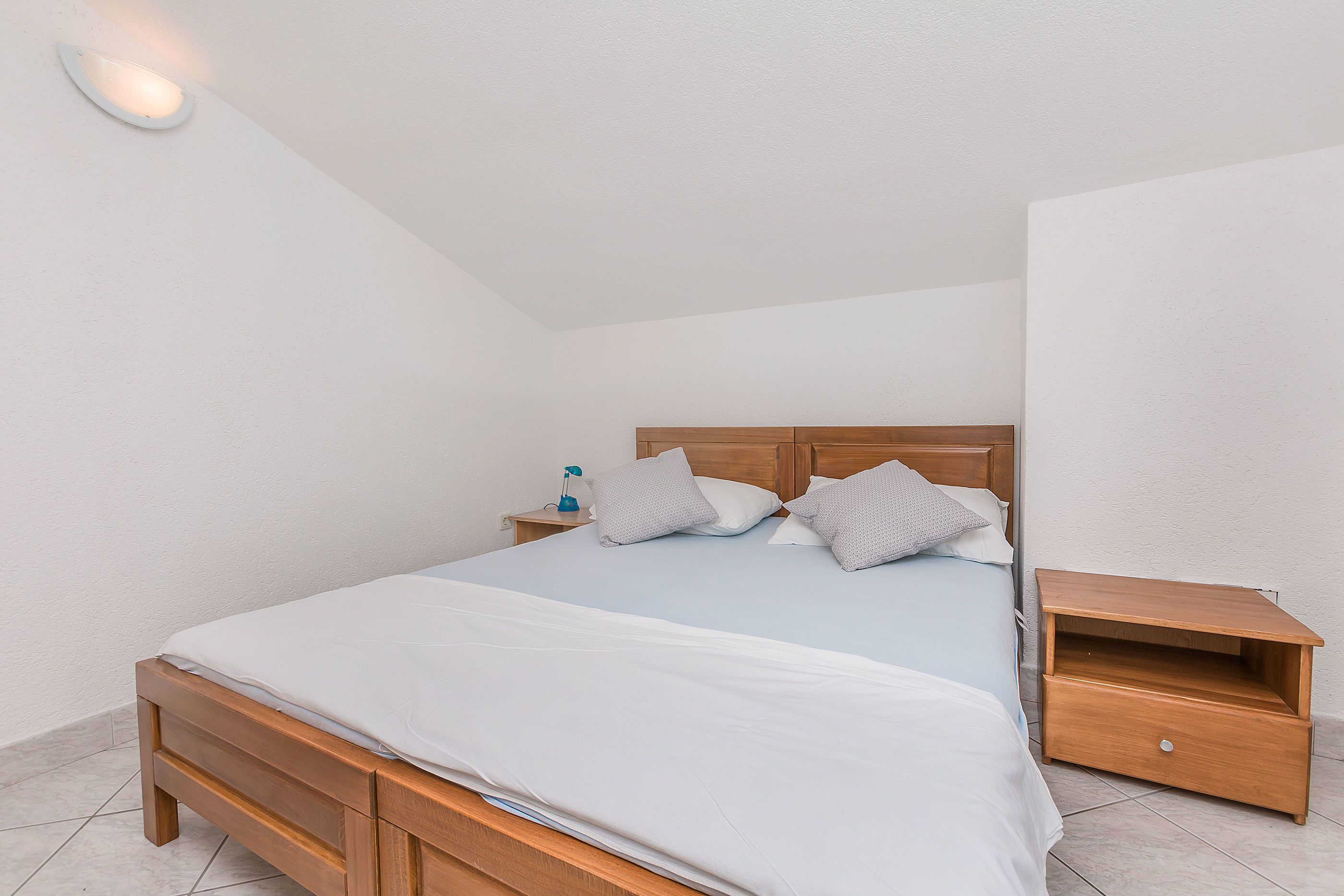 A neatly made bed with a wooden headboard, a bedside table with a lamp, and a small wooden nightstand.