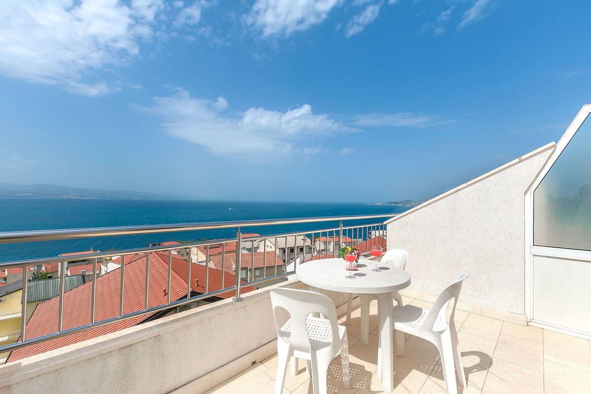 Un balcón con mesa y sillas, con vistas a la costa, edificios y el mar.