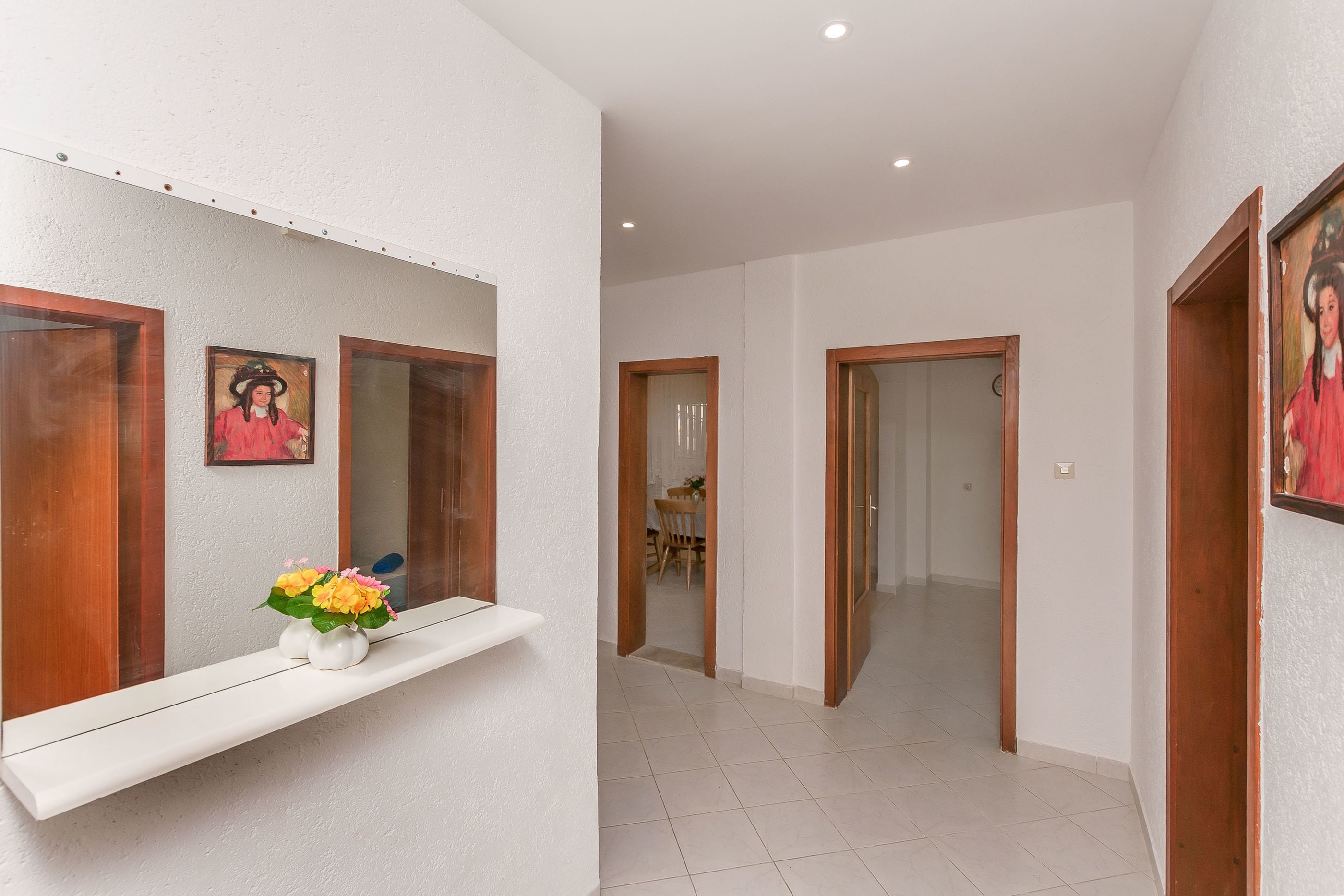 A hallway with white walls, wooden doors, and a white shelf with a vase of flowers.