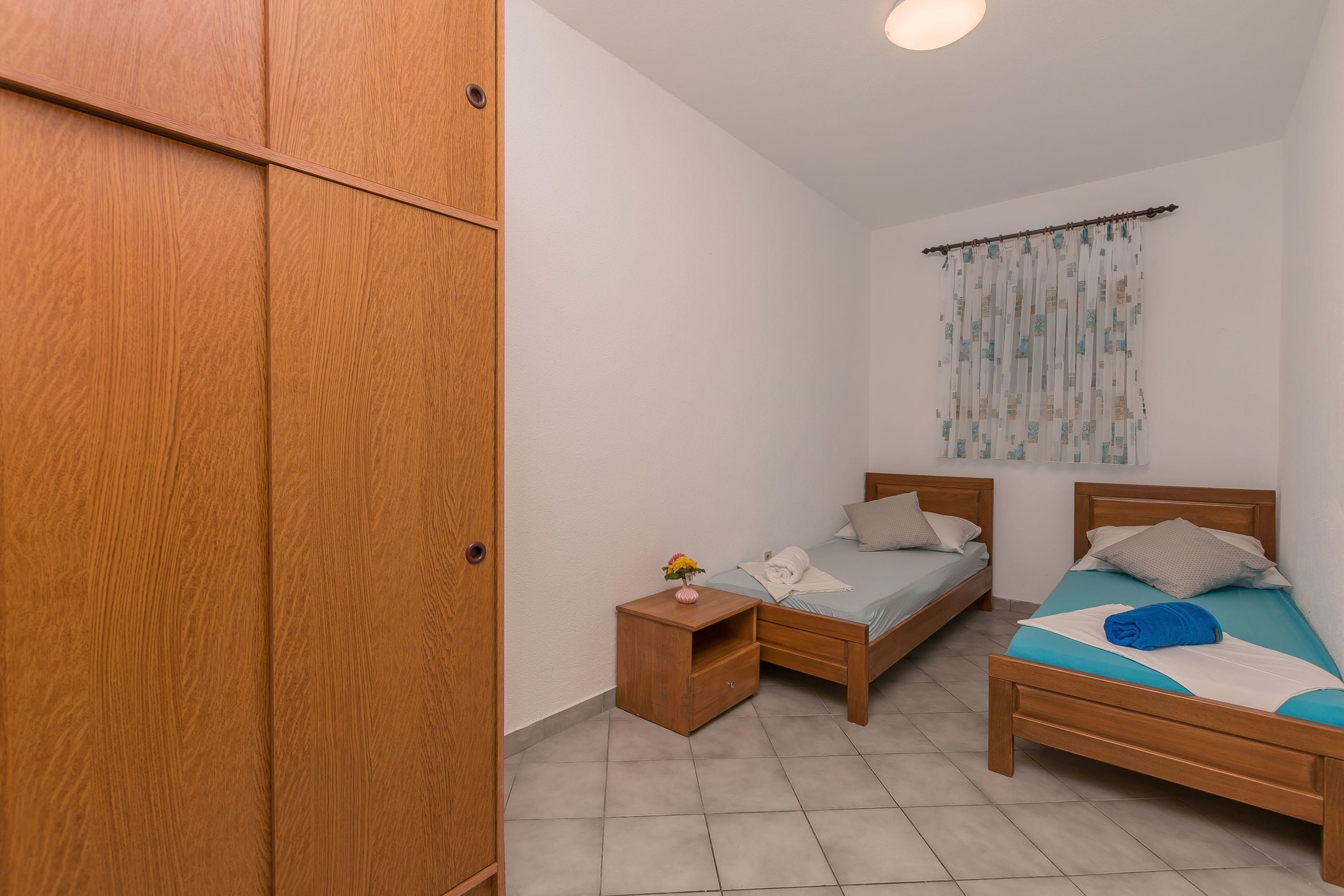 A bedroom with two beds, a wardrobe, and a small bedside table with a vase.
