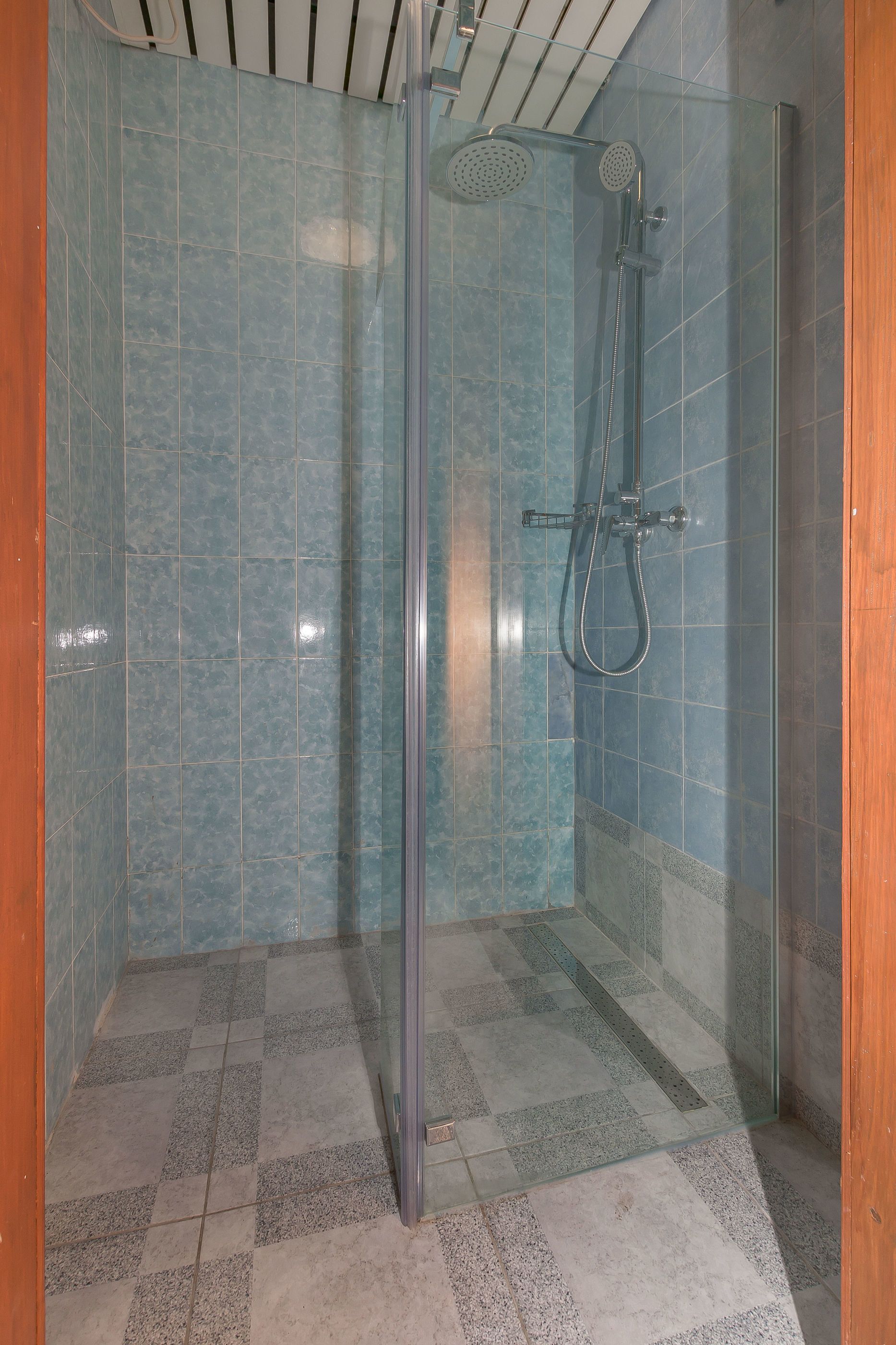 A glass-enclosed shower stall with a handheld showerhead and a wall-mounted faucet.