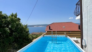 Une piscine avec un escalier, entourée de verdure et offrant une vue sur un bâtiment doté d’un toit rouge.