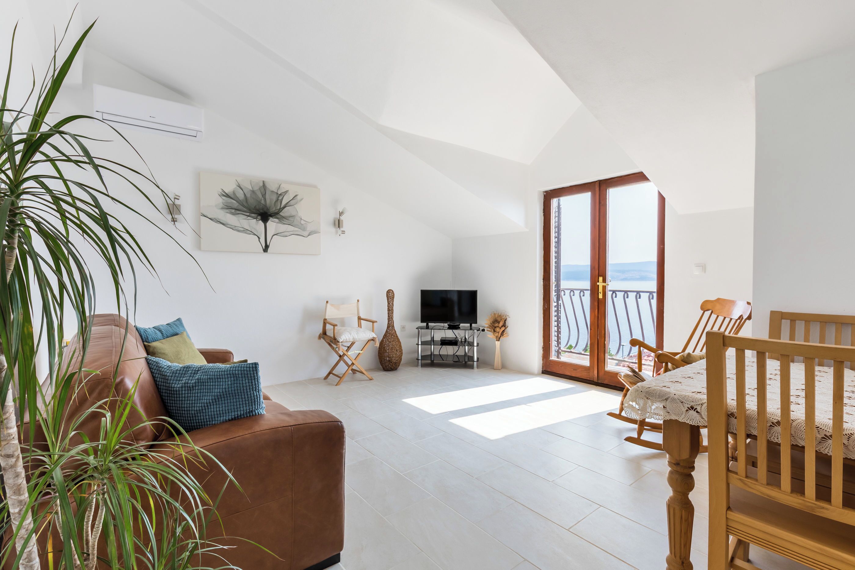 Amplia sala de estar con un sofá de cuero marrón, una mesa de comedor de madera con sillas, un televisor sobre un mueble bajo y un ventanal con vistas.