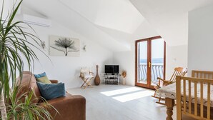Un vaste espace de vie comprenant un canapé en cuir marron, une table à manger en bois avec des chaises, un téléviseur posé sur un meuble et une grande fenêtre offrant une vue dégagée.