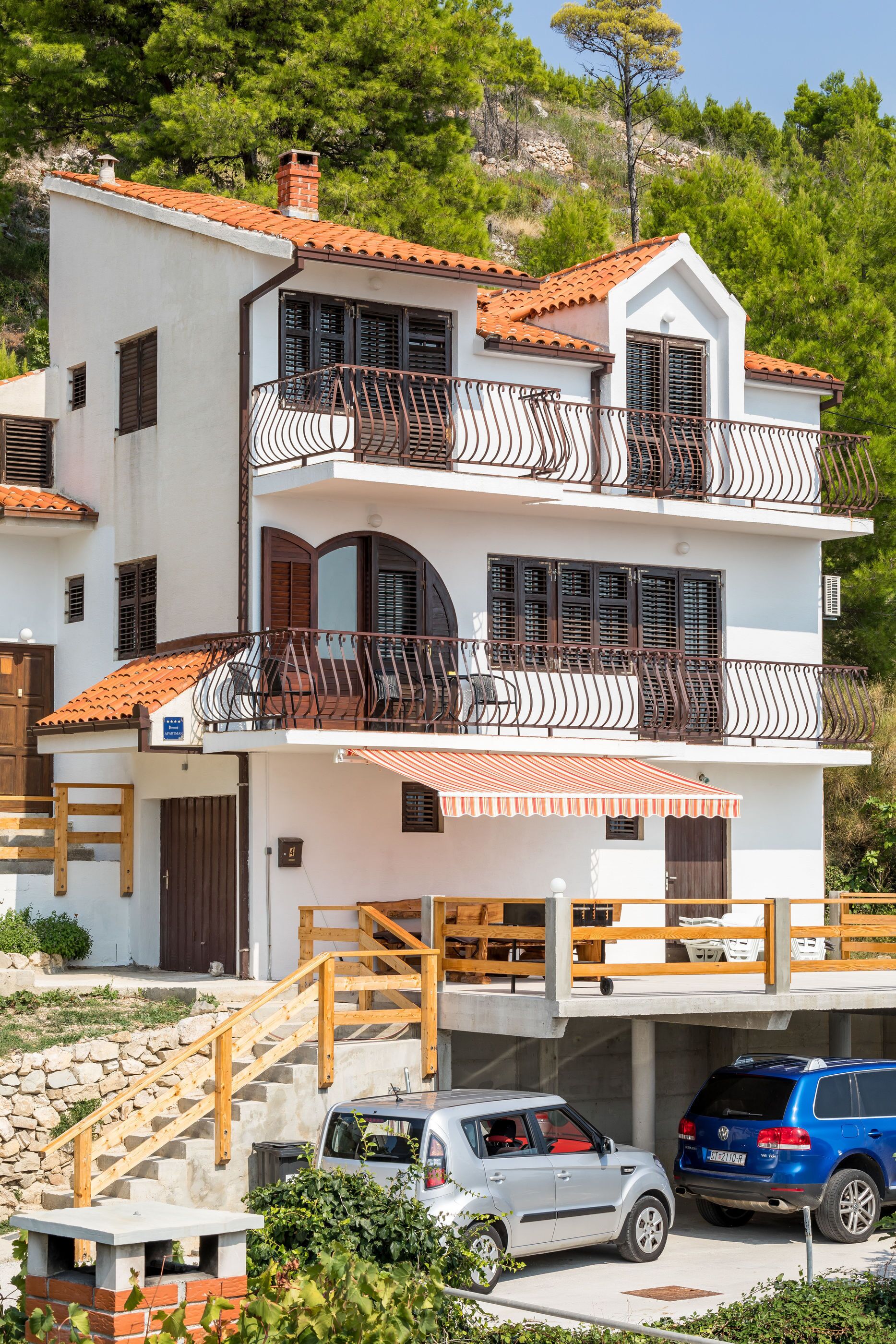 A two-story house with a balcony, a staircase, and a car parked in the driveway.