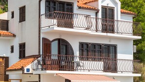 Une maison à deux étages avec un balcon, un escalier et une voiture garée dans l’allée.