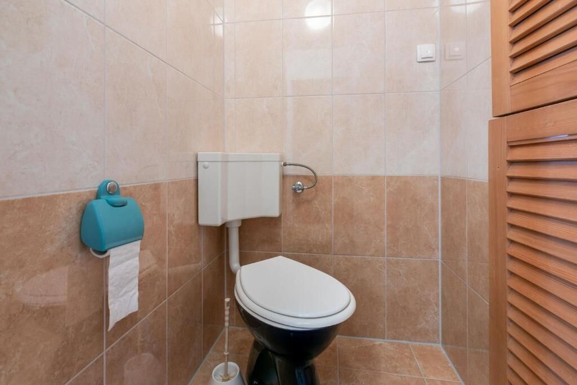 A bathroom with a toilet, a paper towel dispenser, and a flush handle.