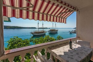 Un balcón con vista al mar, dos barcos y una mesa con una botella y vasos.