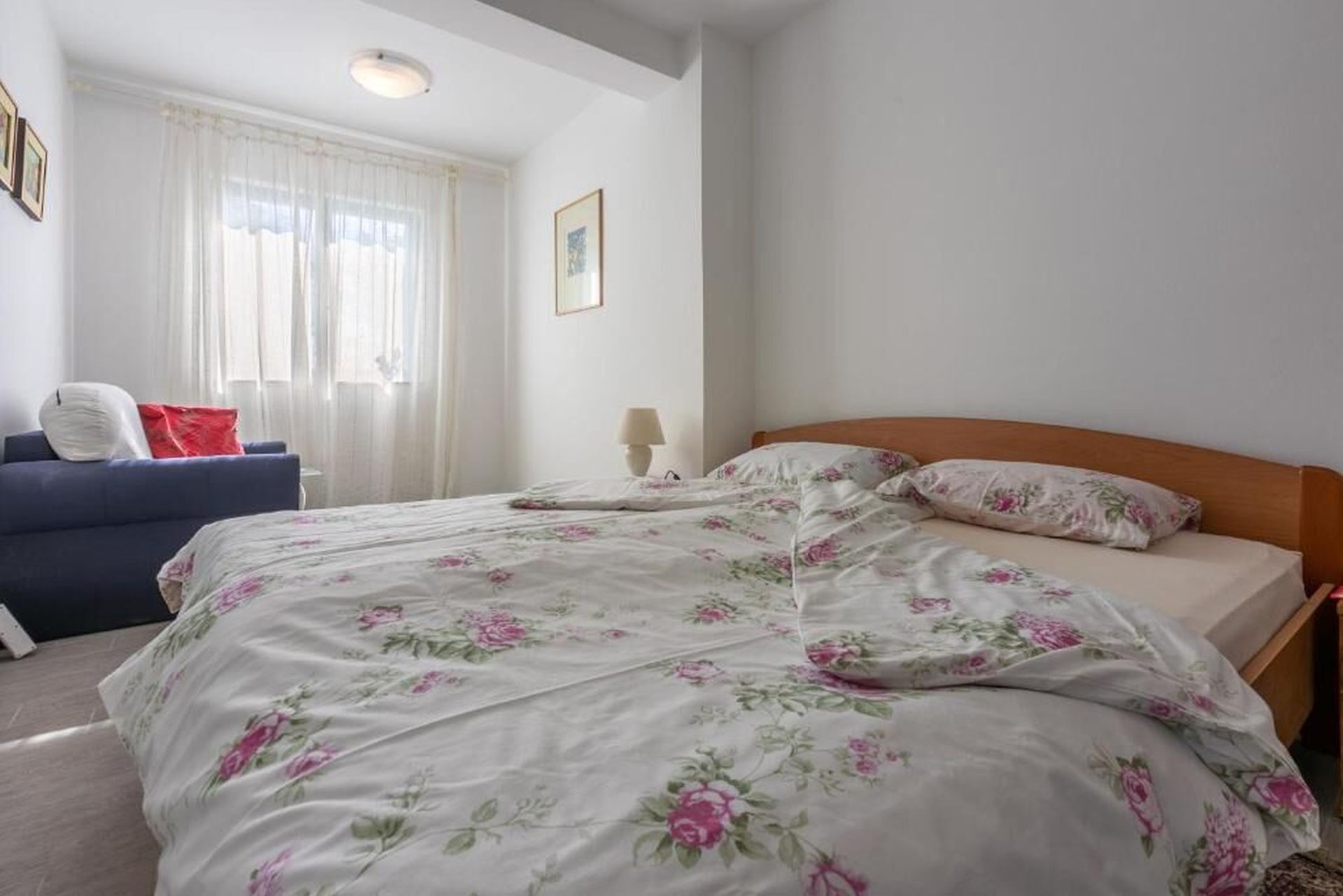 Ein Schlafzimmer mit einem Bett, einem blauen Sofa, einer Lampe und einem Fenster mit Vorhängen.