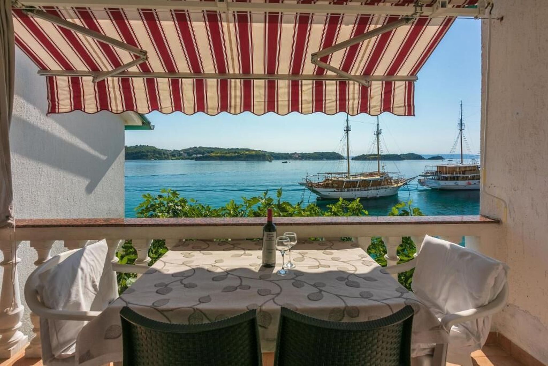 A balcony with a view of the sea, a table with a bottle, and two chairs.