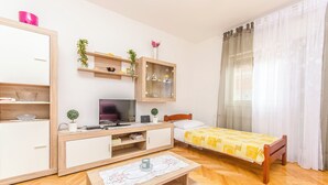 A modern bedroom with a bed, bedside table, TV, wooden wardrobe, and a small shelf with decorative items. - Apartment Sime (Brodarica)