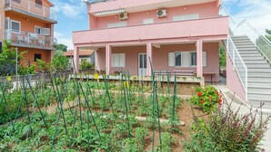 A pink two-story building with a balcony, a garden with vegetables, and a staircase. - Apartment Sime (Brodarica)