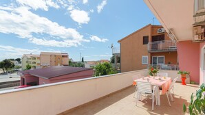 A balcony with a table and chairs, a potted plant, and a view of neighboring buildings. - Apartment Sime (Brodarica)