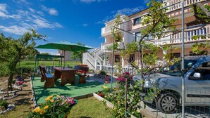 Ein Wohngebäude mit Balkon, einem geparkten Auto davor und einem Gartenbereich mit Tisch und Stühlen.