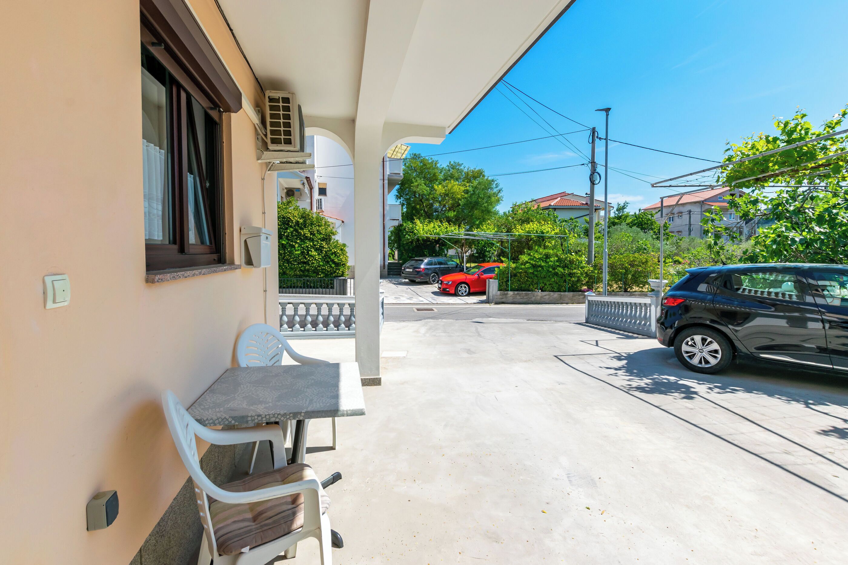 A balcony with a table and chairs, a parked car, and a building in the background.