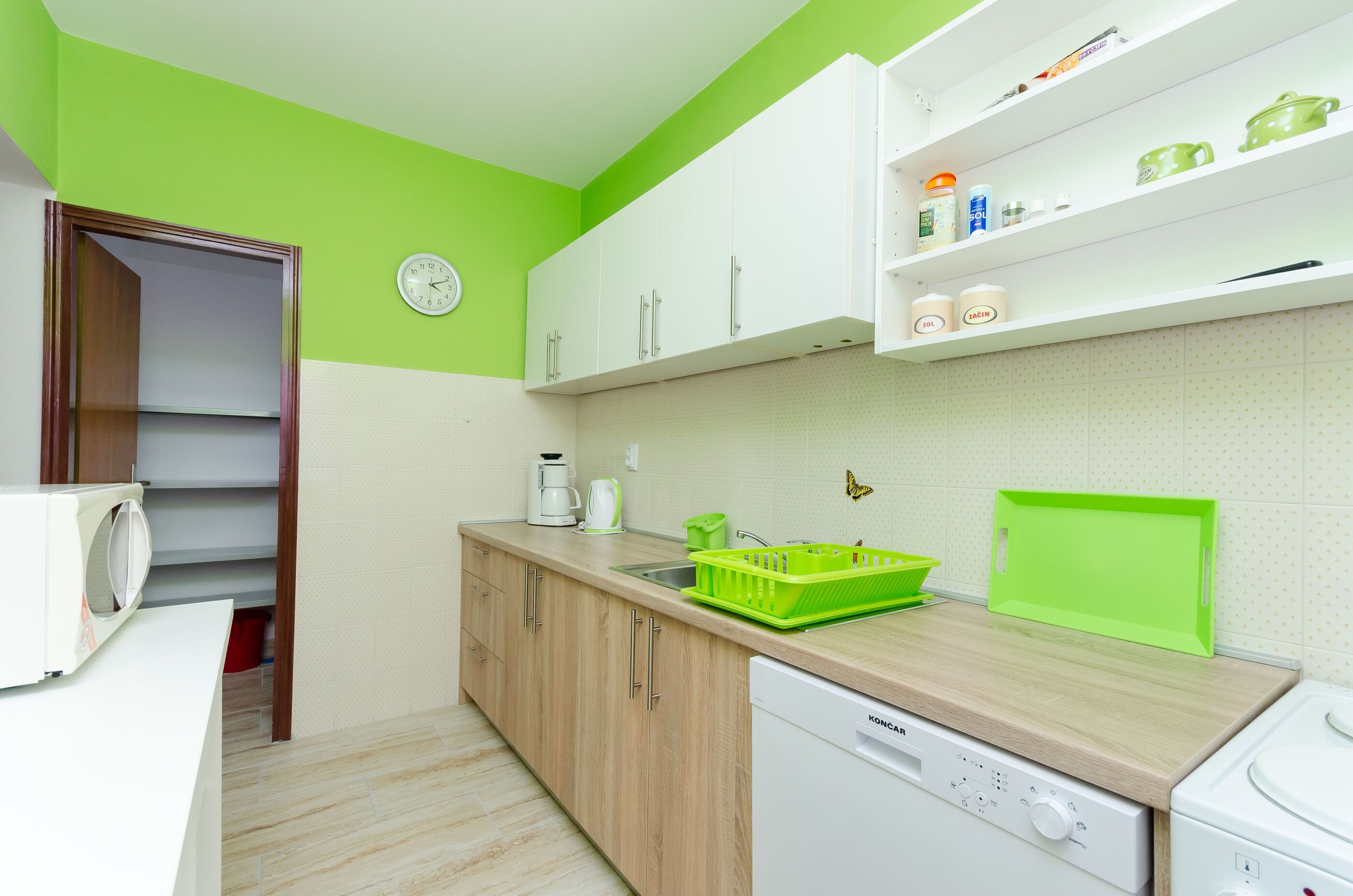 A kitchen with white cabinets, a green wall, a clock, and a dish rack.