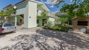 Un edificio a due piani con un balcone, un camino in pietra e un'auto parcheggiata davanti.