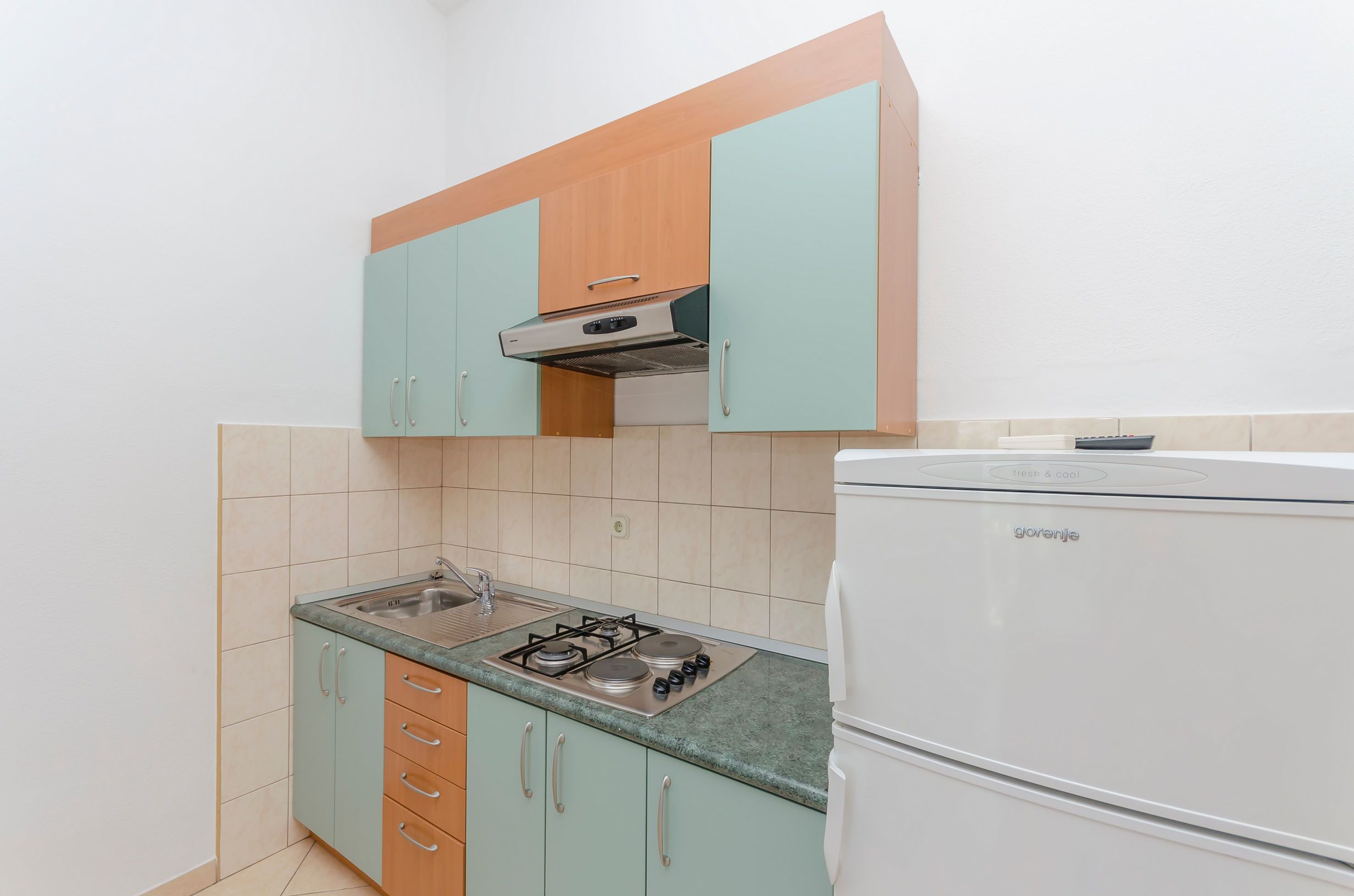 Eine kleine Küche mit einem Gasherd, einem eingebauten Backofen und einem weißen Kühlschrank.