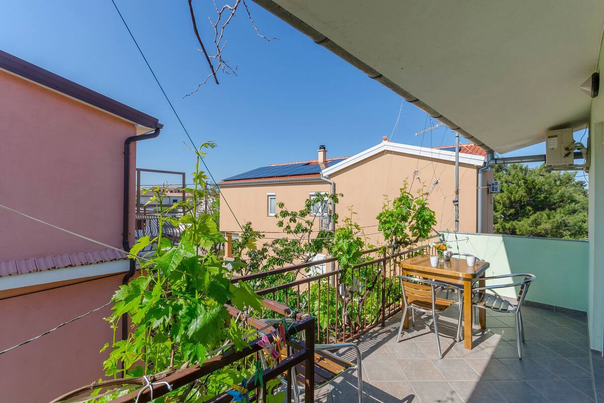 Un balcon avec une table et des chaises, entouré de verdure et avec un bâtiment en arrière-plan.