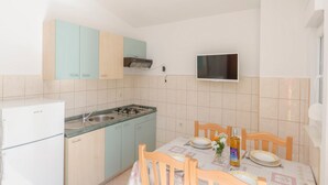 Cucina compatta con piano cottura a gas, forno integrato e microonde. È presente un tavolo da pranzo con sedie e una piccola TV montata a parete.