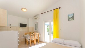 Una stanza con un letto, un tavolo da pranzo con sedie, una TV e una finestra con tende gialle.