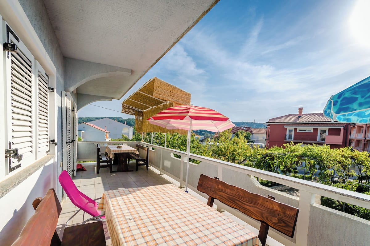 A balcony with a checkered table, a wooden bench, and a striped umbrella.