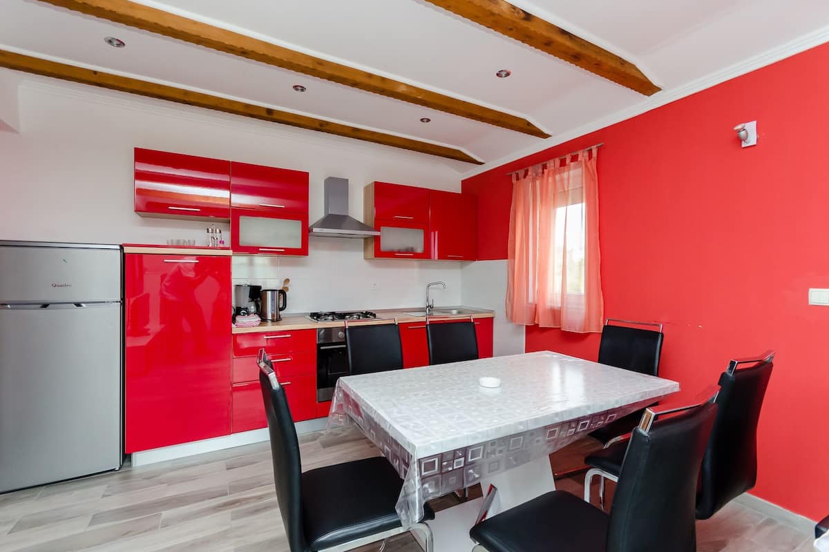 A modern kitchen with red cabinets, a stainless steel refrigerator, and a dining area with a table and chairs.