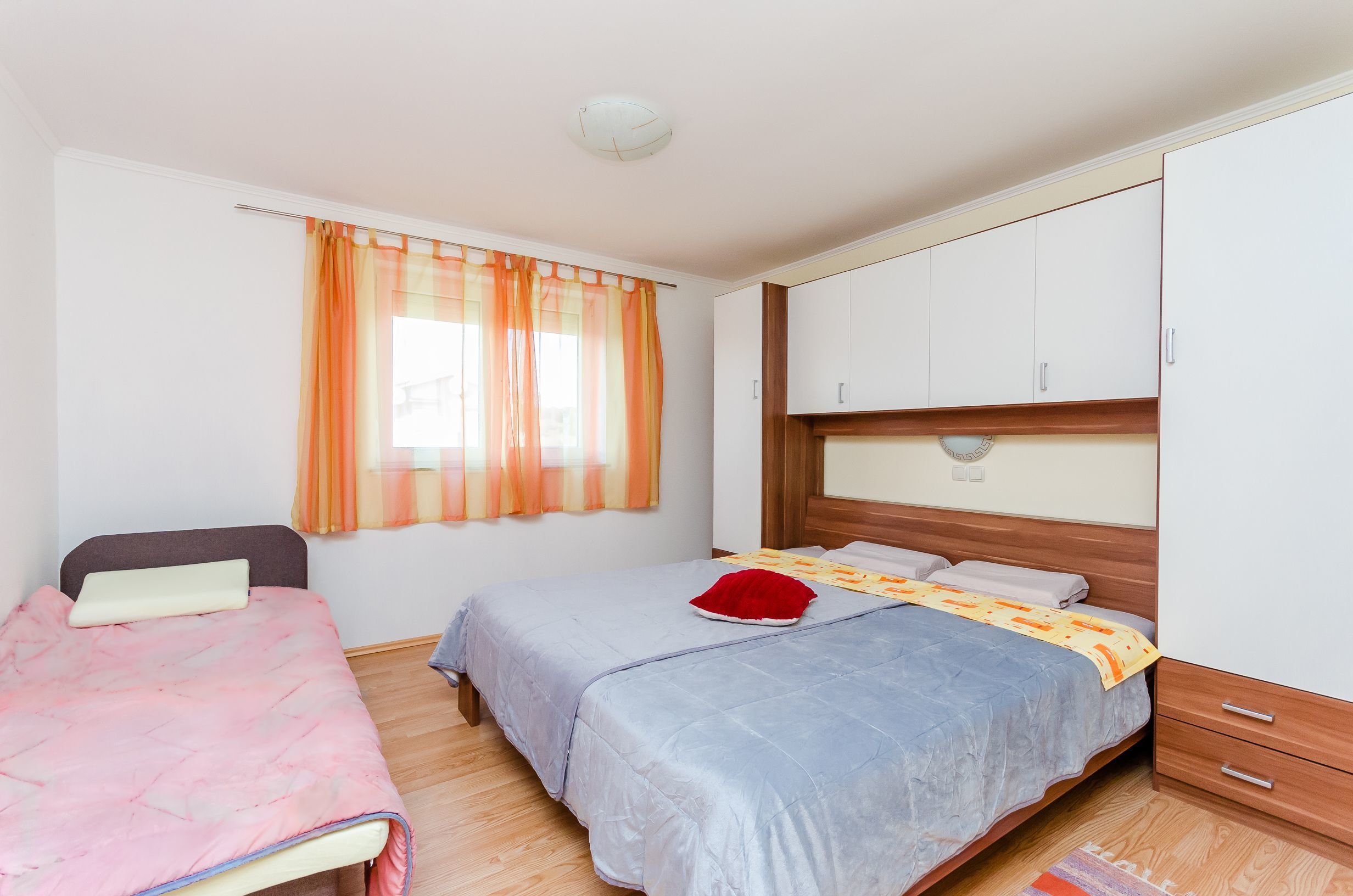 A bedroom with two beds, a wardrobe, and a window with curtains.