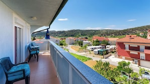 Un balcón con mobiliario exterior, vistas a un barrio residencial y cielo despejado.