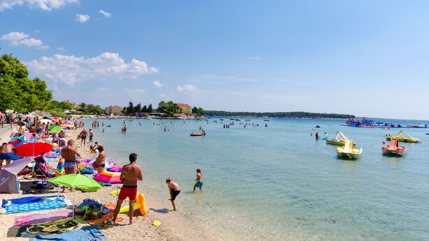 Ein voller Strand mit badenden und sonnenden Menschen.