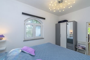Un dormitorio con cama, armario, ventana y lámpara en el techo.
