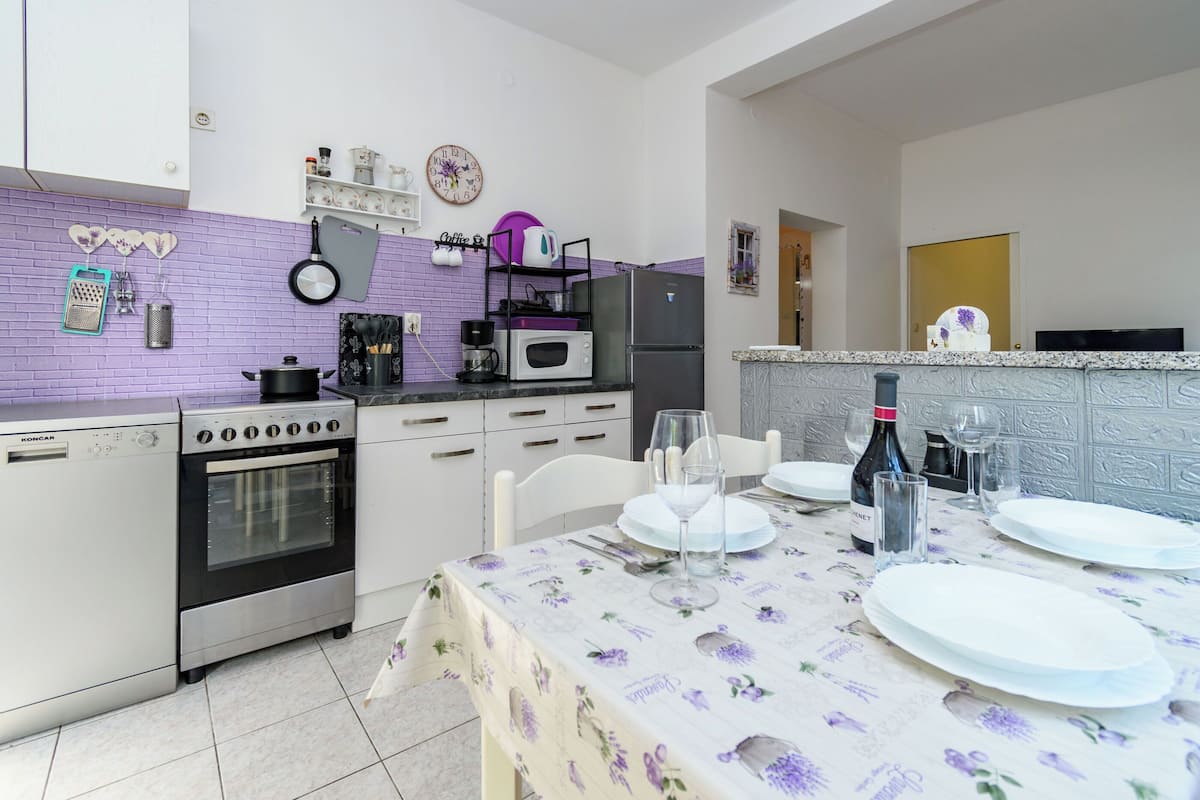 A kitchen with a dining table set for two, a refrigerator, oven, and microwave.